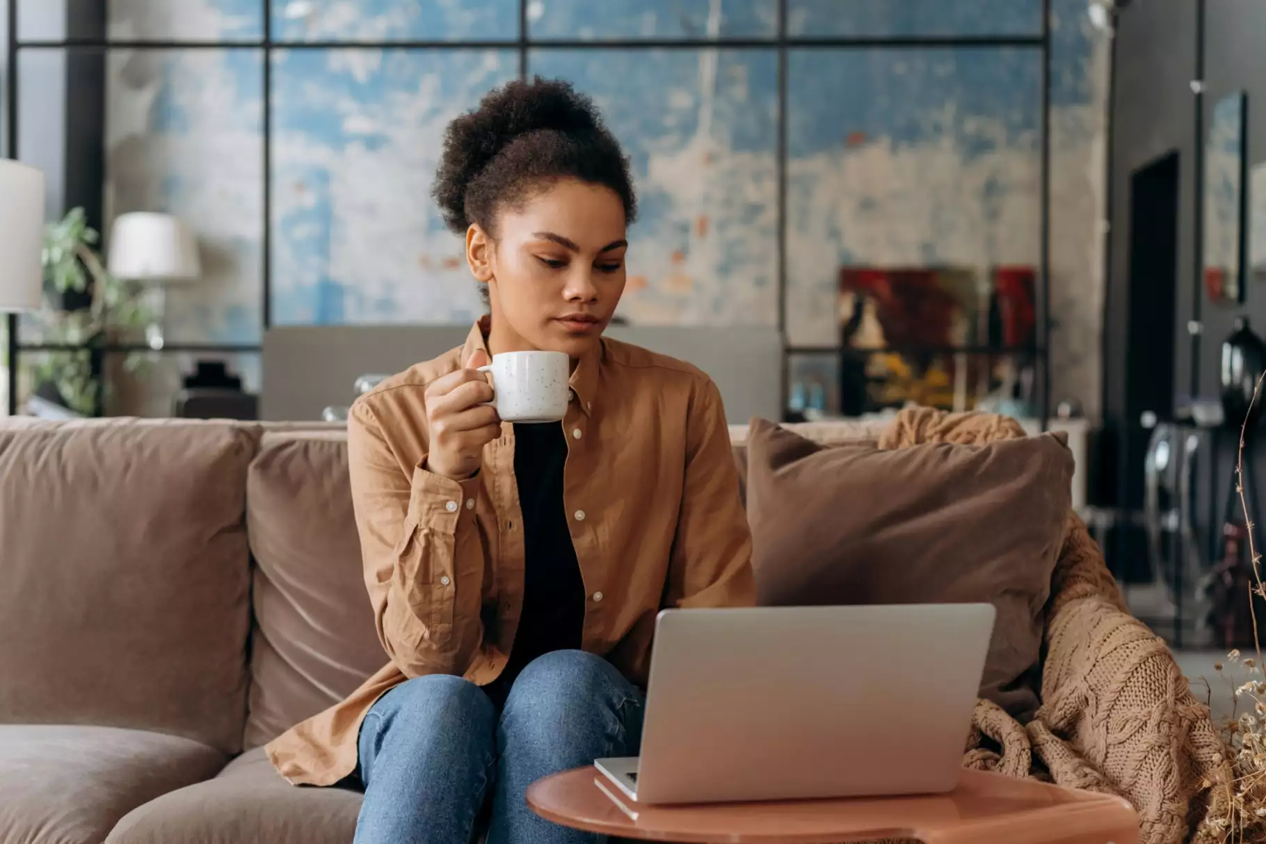 vrouw drinkt kopje koffie op bank met laptop